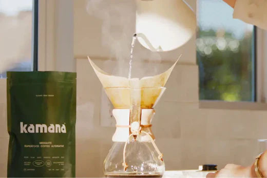 Mesquite coffee being brewed in a Chemex with hot water poured over a filter, alongside a Kamana coffee alternative bag